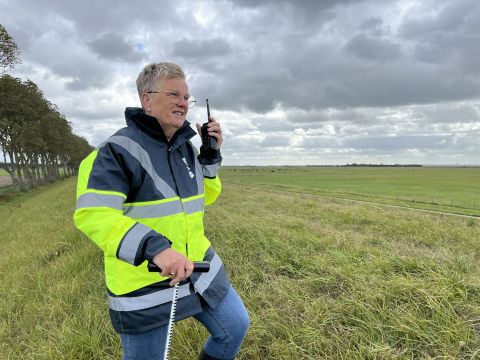Dijkwacht Tea Both op een dijk met een portofoon en peilstok